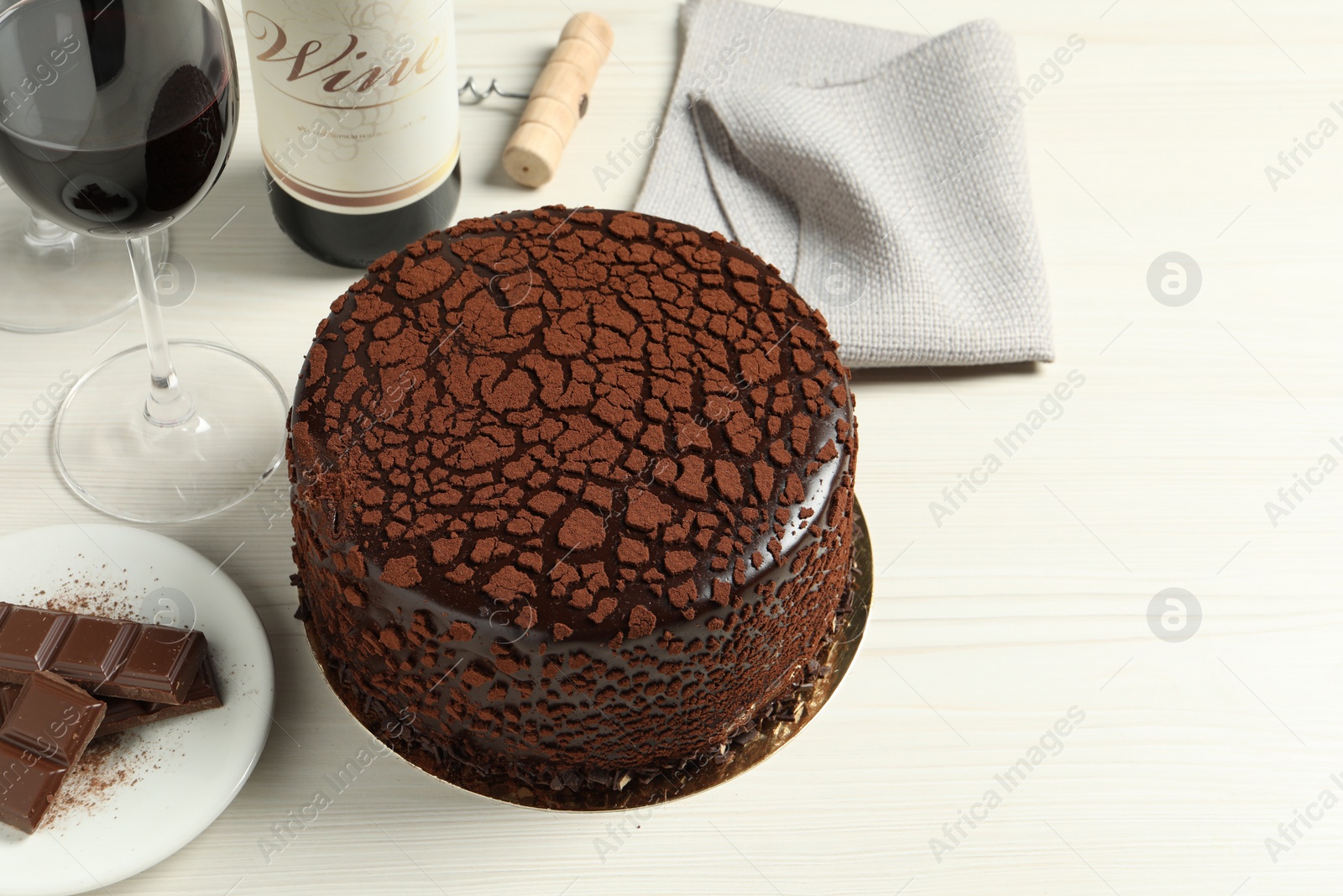 Photo of Delicious truffle cake, chocolate pieces and red wine on light wooden table, space for text