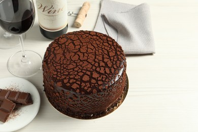 Delicious truffle cake, chocolate pieces and red wine on light wooden table, space for text