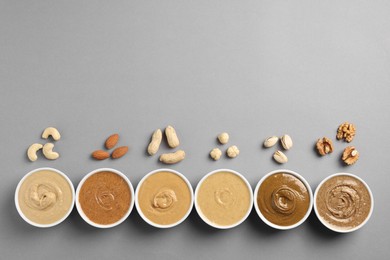 Photo of Many tasty nut butters in bowls and nuts on grey table, flat lay. Space for text