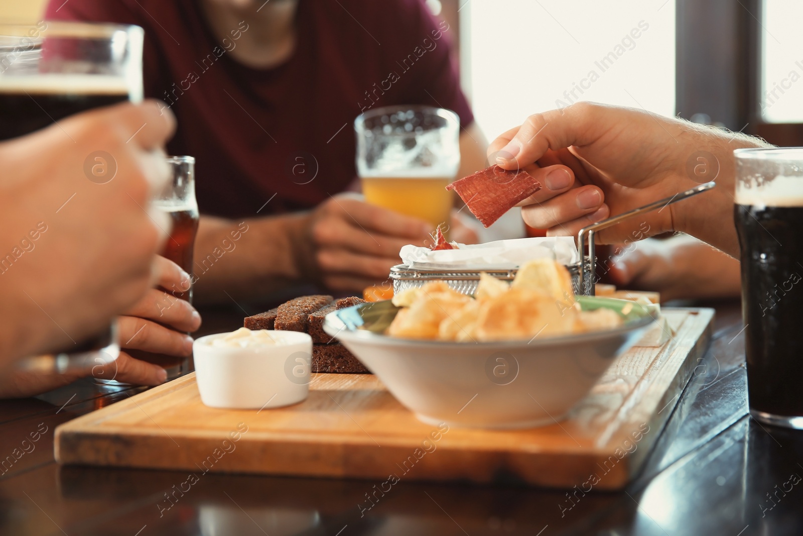 Photo of Friends drinking beer and eating snacks at table in pub