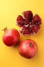 Photo of Whole and cut fresh pomegranates on yellow background, flat lay