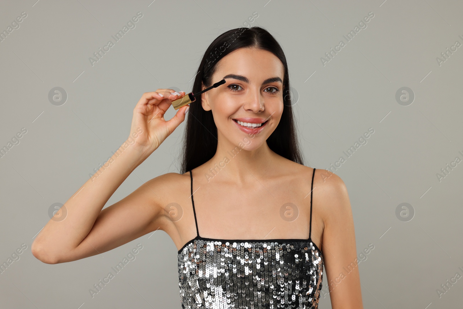 Photo of Beautiful young woman applying mascara on grey background