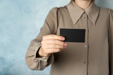 Woman holding blank business card on light blue background, closeup. Mockup for design