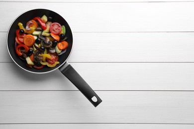 Photo of Mix of tasty vegetables in pan on white wooden table, top view. Space for text