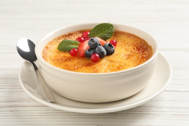 Photo of Delicious creme brulee with fresh berries on white wooden table, closeup