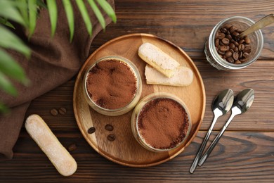 Photo of Delicious tiramisu in glasses served on wooden table, flat lay