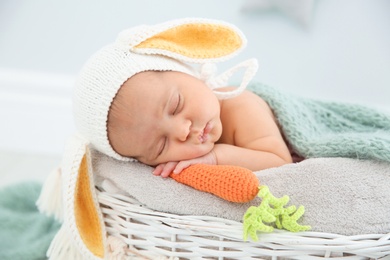 Photo of Adorable newborn child wearing bunny ears hat in baby nest indoors