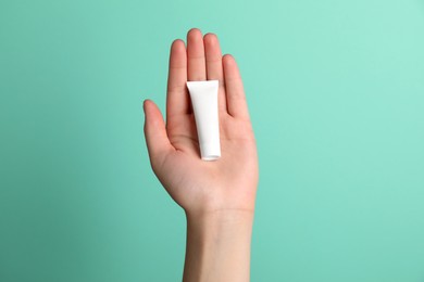 Woman holding tube of face cream on turquoise background, closeup