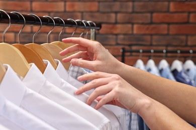 Photo of Dry-cleaning service. Woman taking shirt from rack against brick wall, closeup