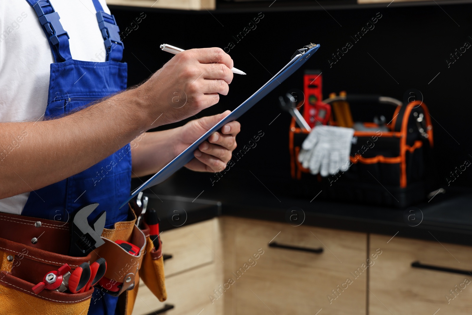 Photo of Professional plumber with clipboard and tool belt indoors, closeup. Space for text