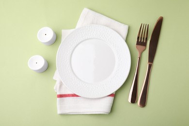 Photo of Clean plate with cutlery and napkin on light green background, flat lay
