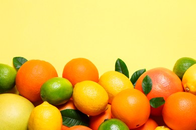 Different fresh citrus fruits and leaves on yellow background, flat lay. Space for text