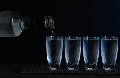 Photo of Pouring vodka from bottle in glass on black table