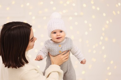 Photo of Happy young mother with her cute baby against blurred festive lights, space for text. Winter holiday