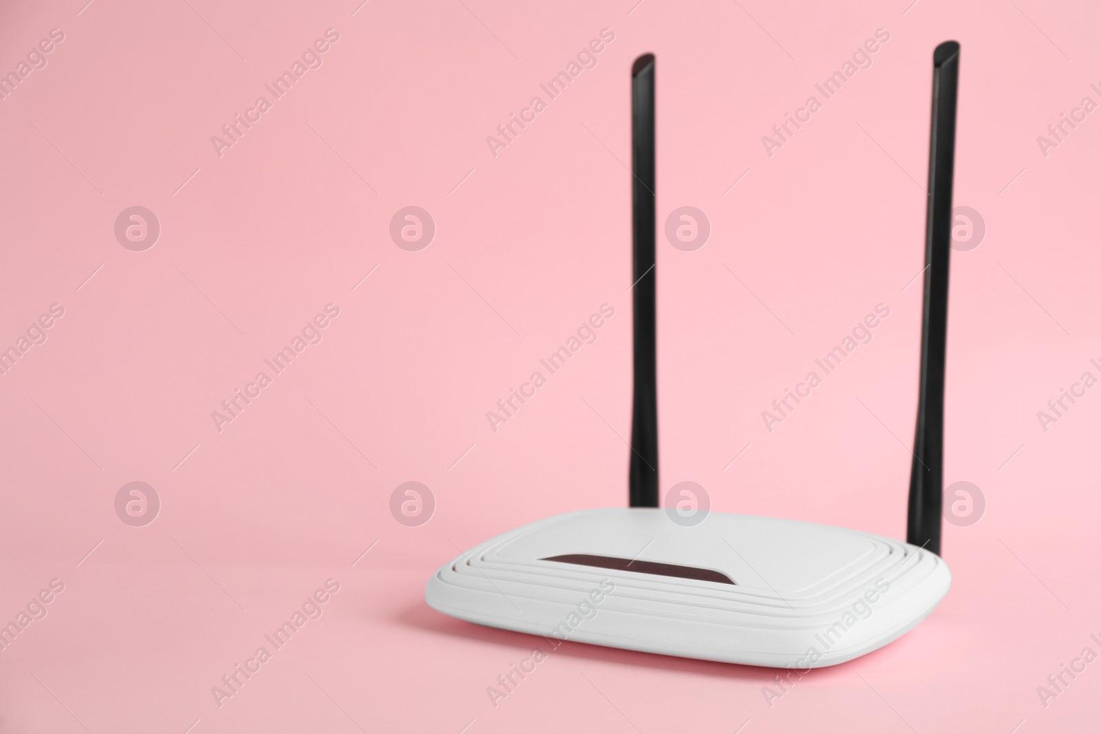 Photo of Modern Wi-Fi router on light pink background. Space for text