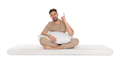 Man with pillow sitting on soft mattress and pointing upwards against white background