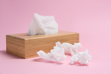 Photo of Holder with paper tissues and used crumpled napkins on pink background