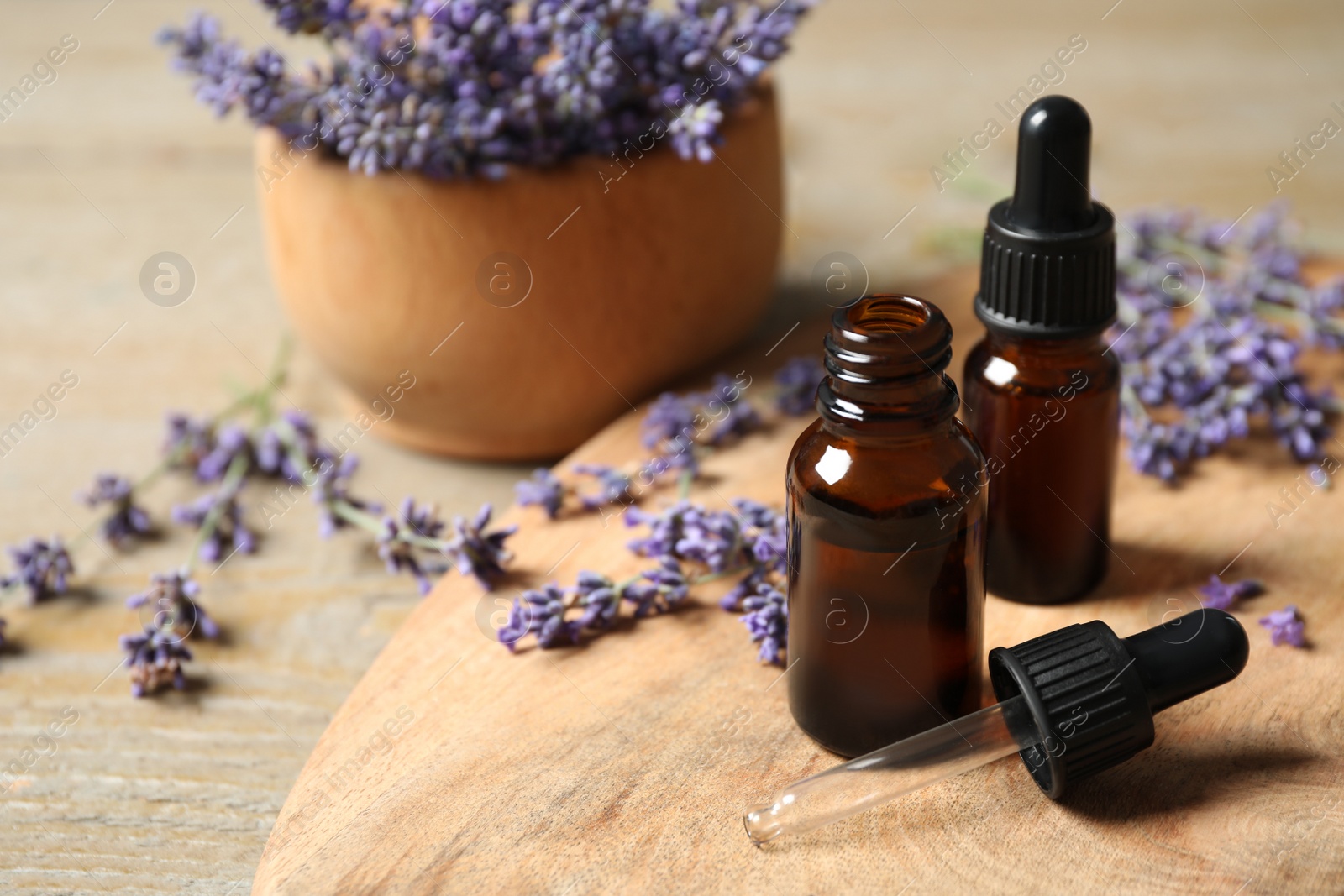 Photo of Bottles of essential oil and lavender flowers on wooden table