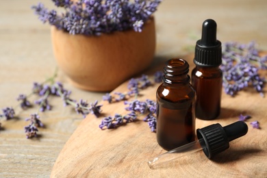 Bottles of essential oil and lavender flowers on wooden table