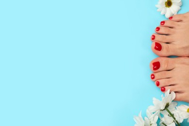 Photo of Woman with stylish red toenails after pedicure procedure and chamomile flowers on light blue background, top view. Space for text