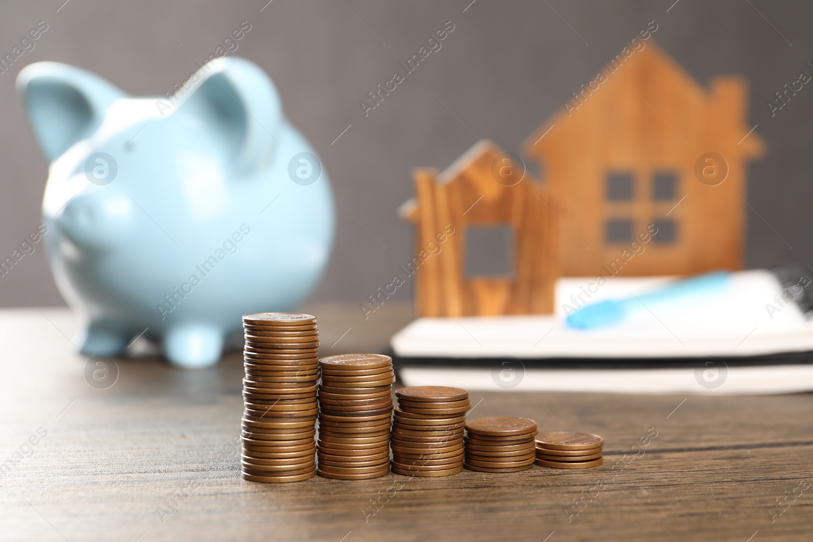 Photo of House models, stacked coins, piggy bank and notebook on wooden table, selective focus