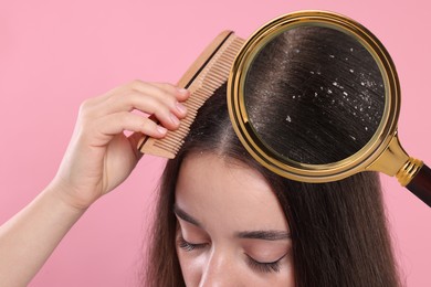 Woman suffering from dandruff on pink background, closeup. View through magnifying glass on hair with flakes