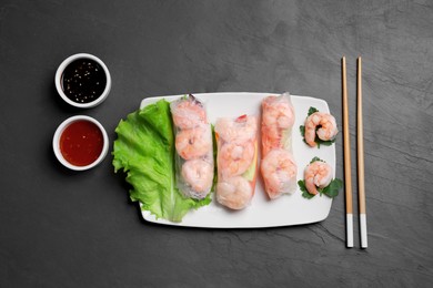 Photo of Delicious spring rolls with shrimps wrapped in rice paper served on black table, flat lay
