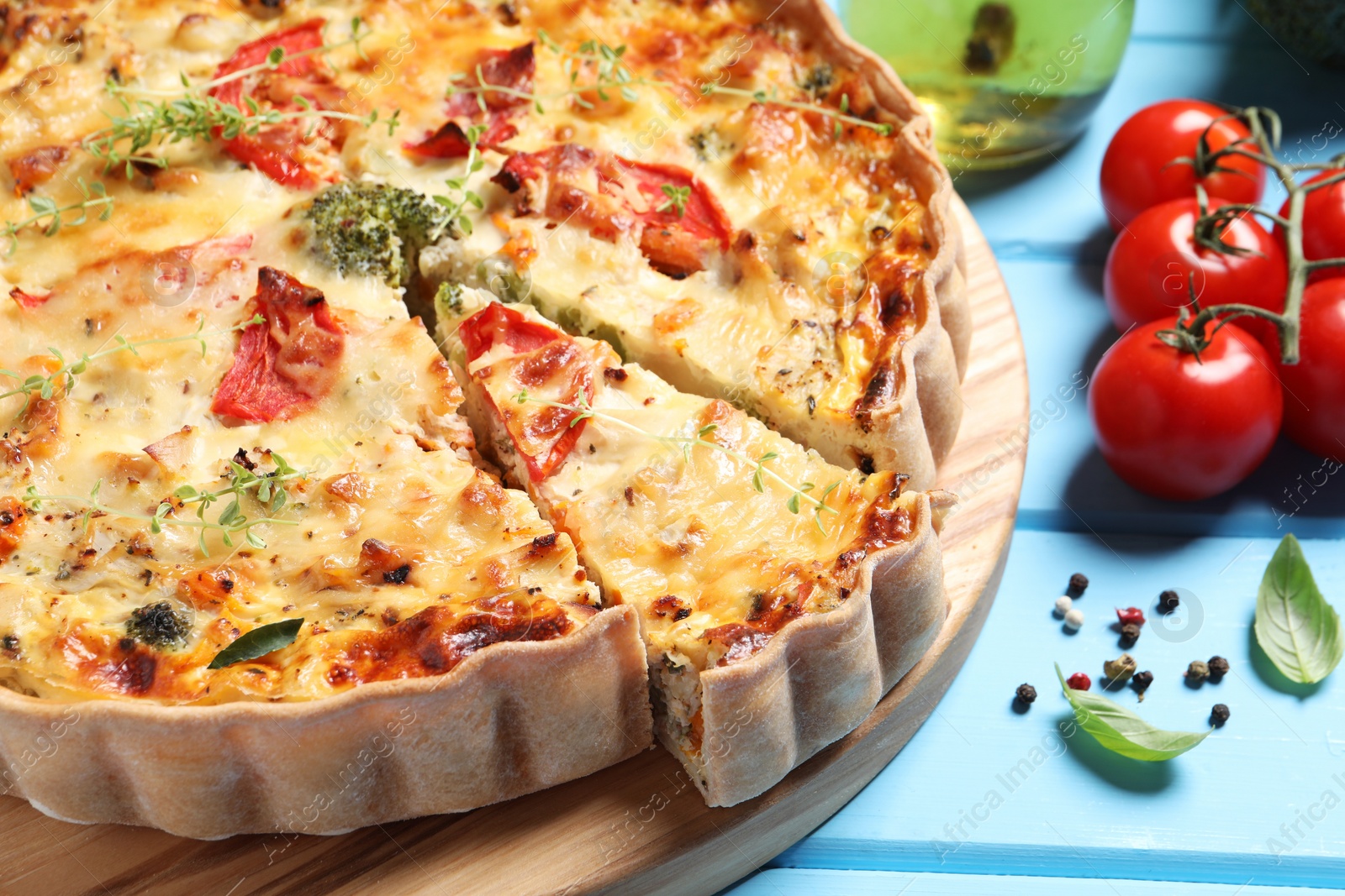 Photo of Tasty quiche with tomatoes, microgreens and cheese served on light blue wooden table, closeup