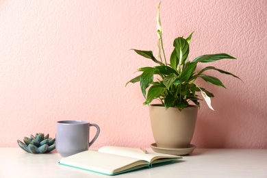 Photo of Composition with peace lily and notebook on table against color wall. Space for text