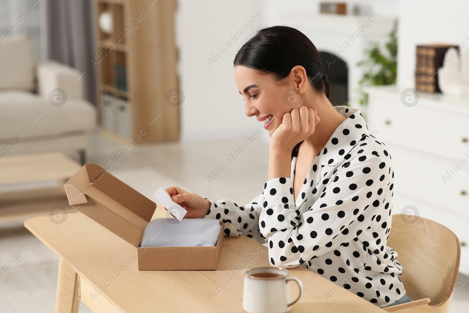Photo of Happy woman holding greeting card near parcel with Christmas gift at home