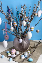 Photo of Beautiful willow branches with painted eggs in vase on white wooden table. Easter decor