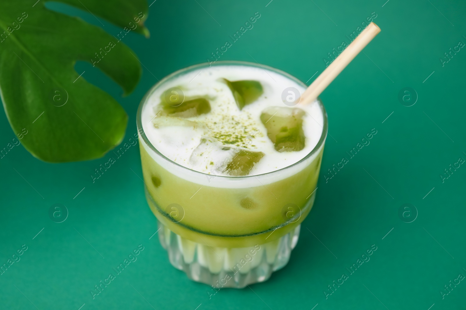 Photo of Glass of tasty iced matcha latte and leaf on green background, closeup