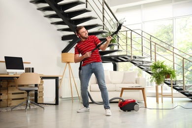 Photo of Young man having fun while vacuuming in living room