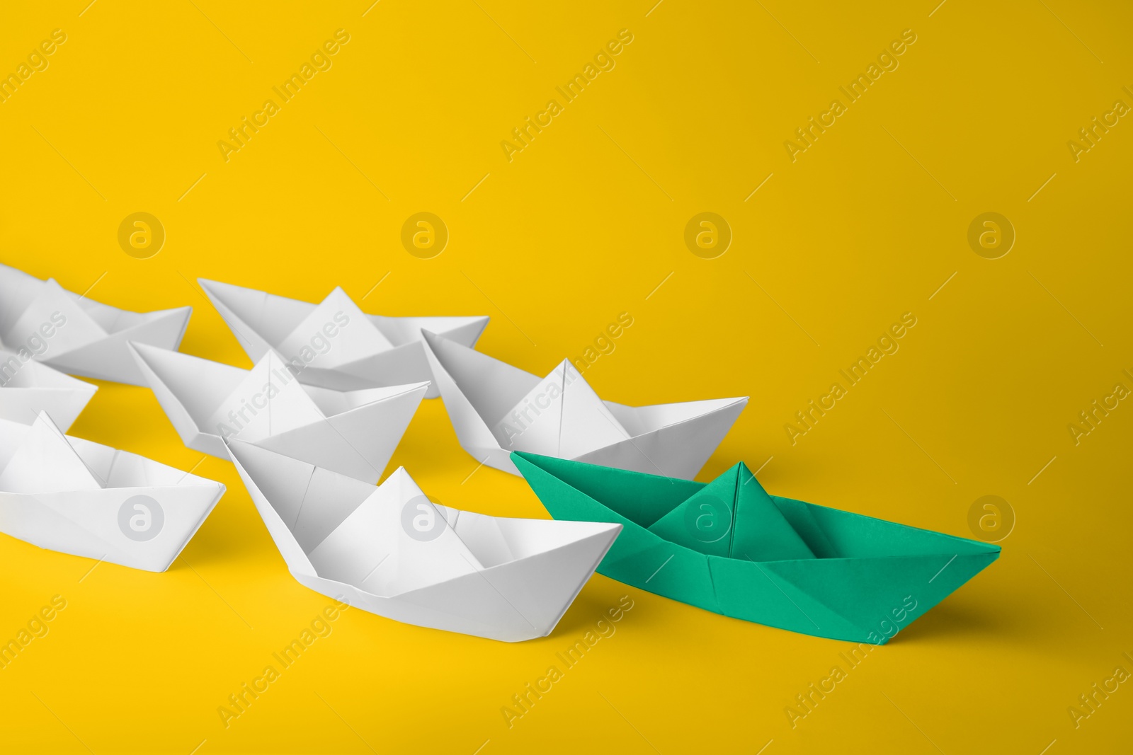 Photo of Group of paper boats following green one on yellow background. Leadership concept