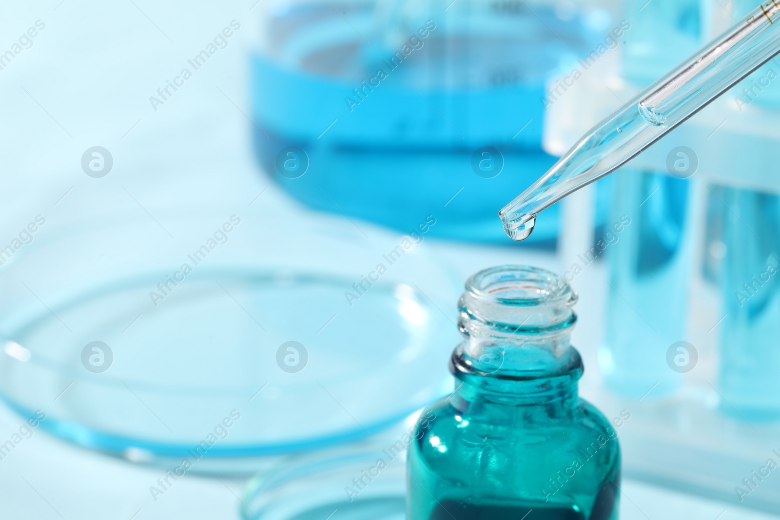Photo of Dripping liquid from pipette into bottle on blurred background, closeup. Space for text