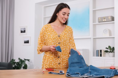 Photo of Happy woman holding jeans and cut hem at table indoors