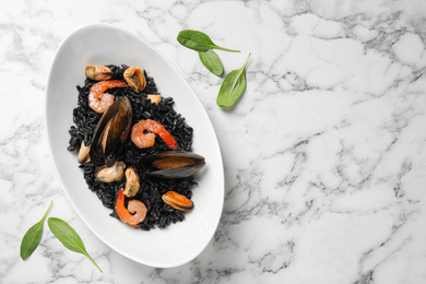 Delicious black risotto with seafood on white marble table, flat lay. Space for text