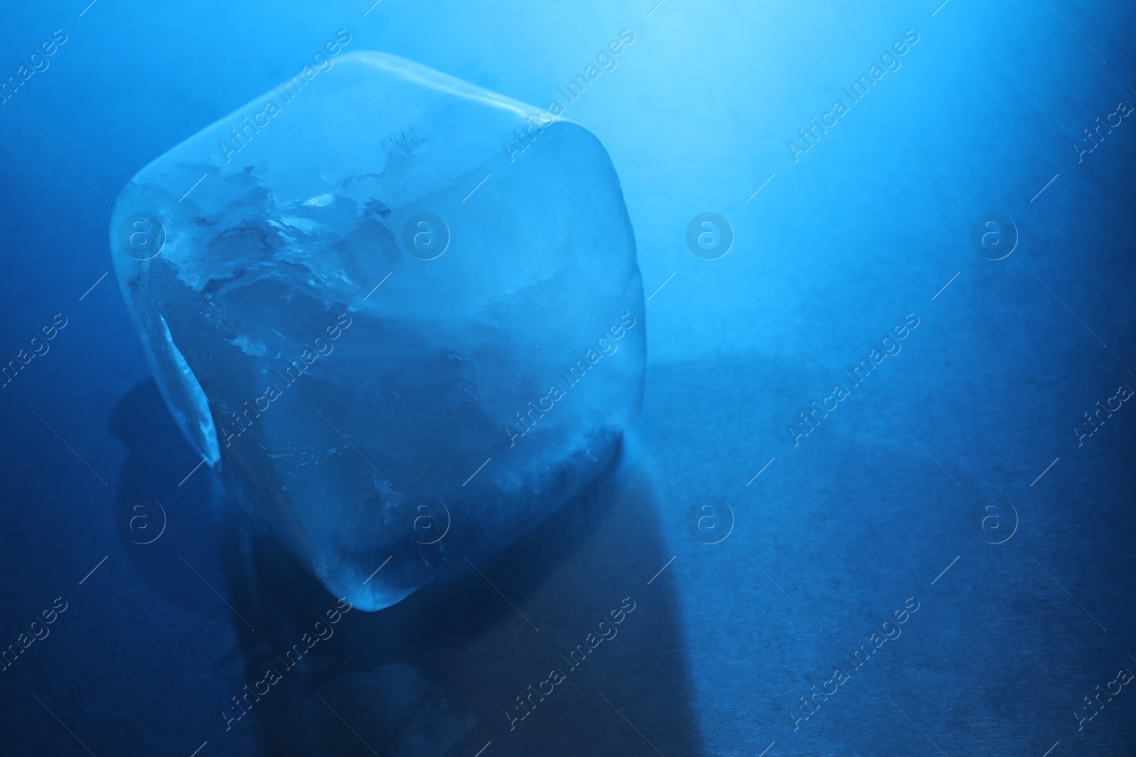 Photo of One crystal clear ice cube on light blue background, closeup and space for text. Color tone effect