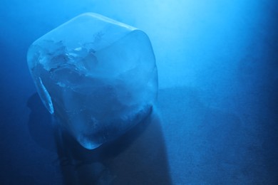 One crystal clear ice cube on light blue background, closeup and space for text. Color tone effect