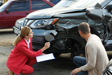 Photo of Man reporting and insurance agent filling claim form near broken car outdoors