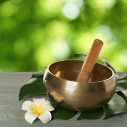 Image of Golden singing bowl, mallet, leaf and flower on grey wooden table outdoors