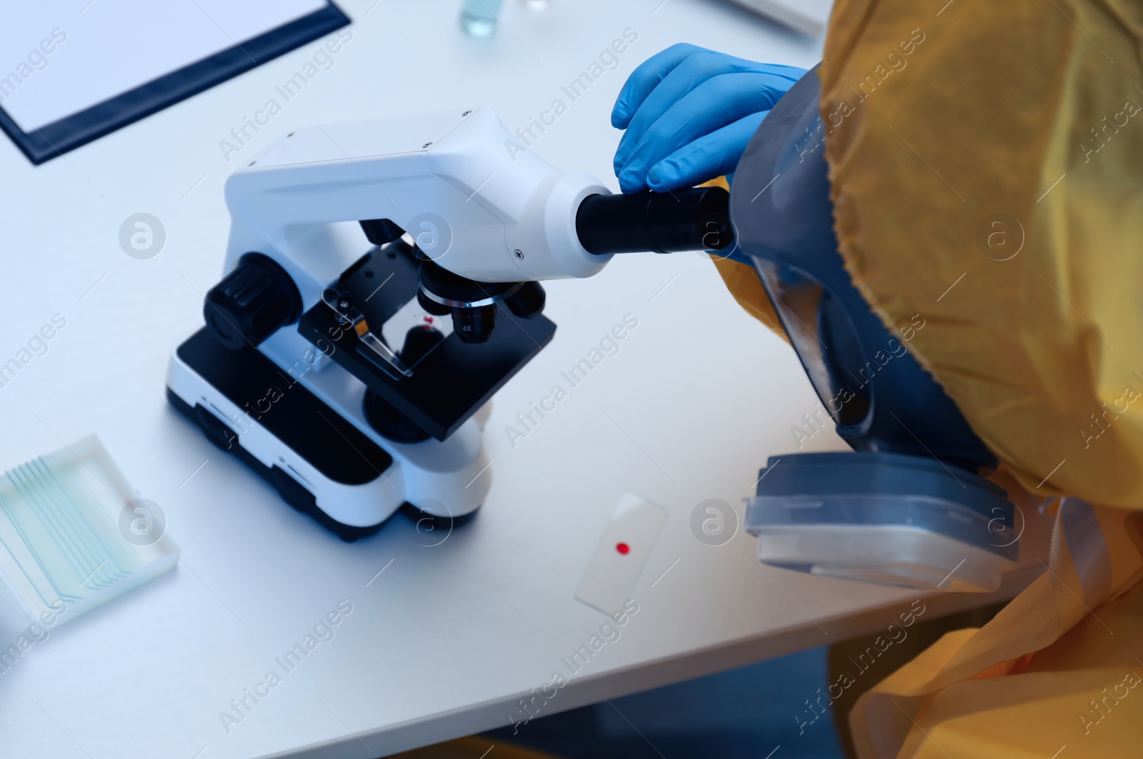 Photo of Scientist in chemical protective suit using microscope at table, closeup. Virus research