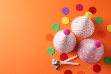 Photo of Party hats and other bright decor elements on orange background, flat lay. Space for text