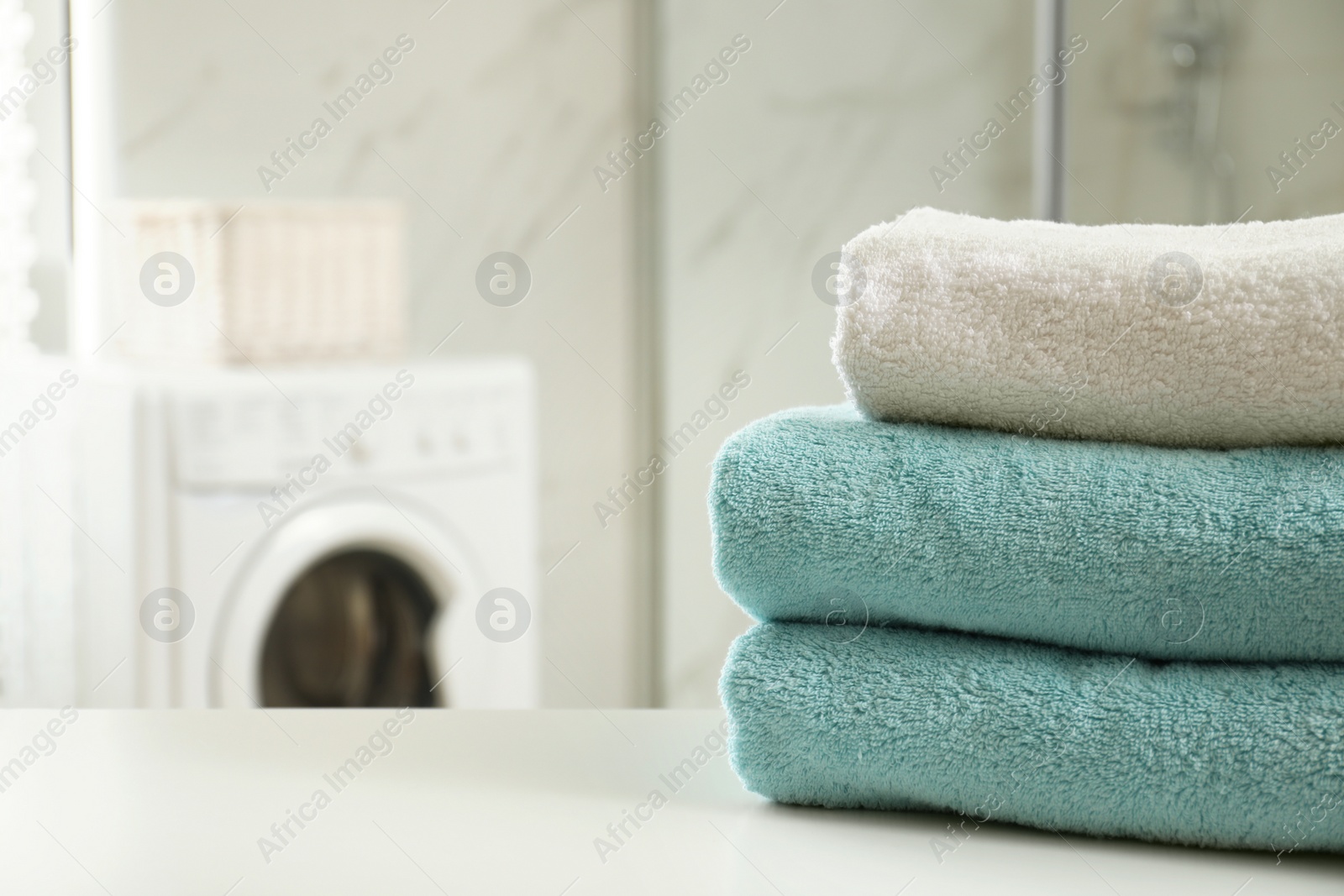 Photo of Stack of clean towels on table in laundry room. Space for text