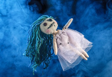 Female voodoo doll with pins and smoke on blue  background