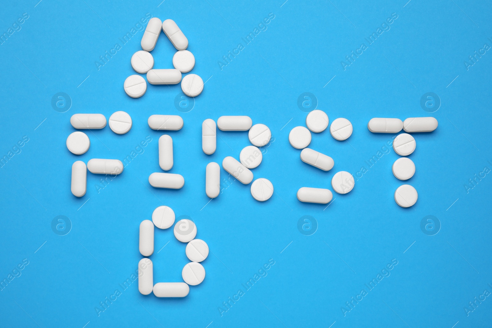 Photo of Words First Aid made of pills on light blue background, flat lay