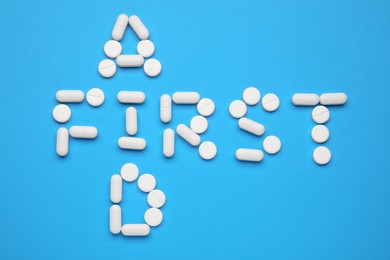 Photo of Words First Aid made of pills on light blue background, flat lay