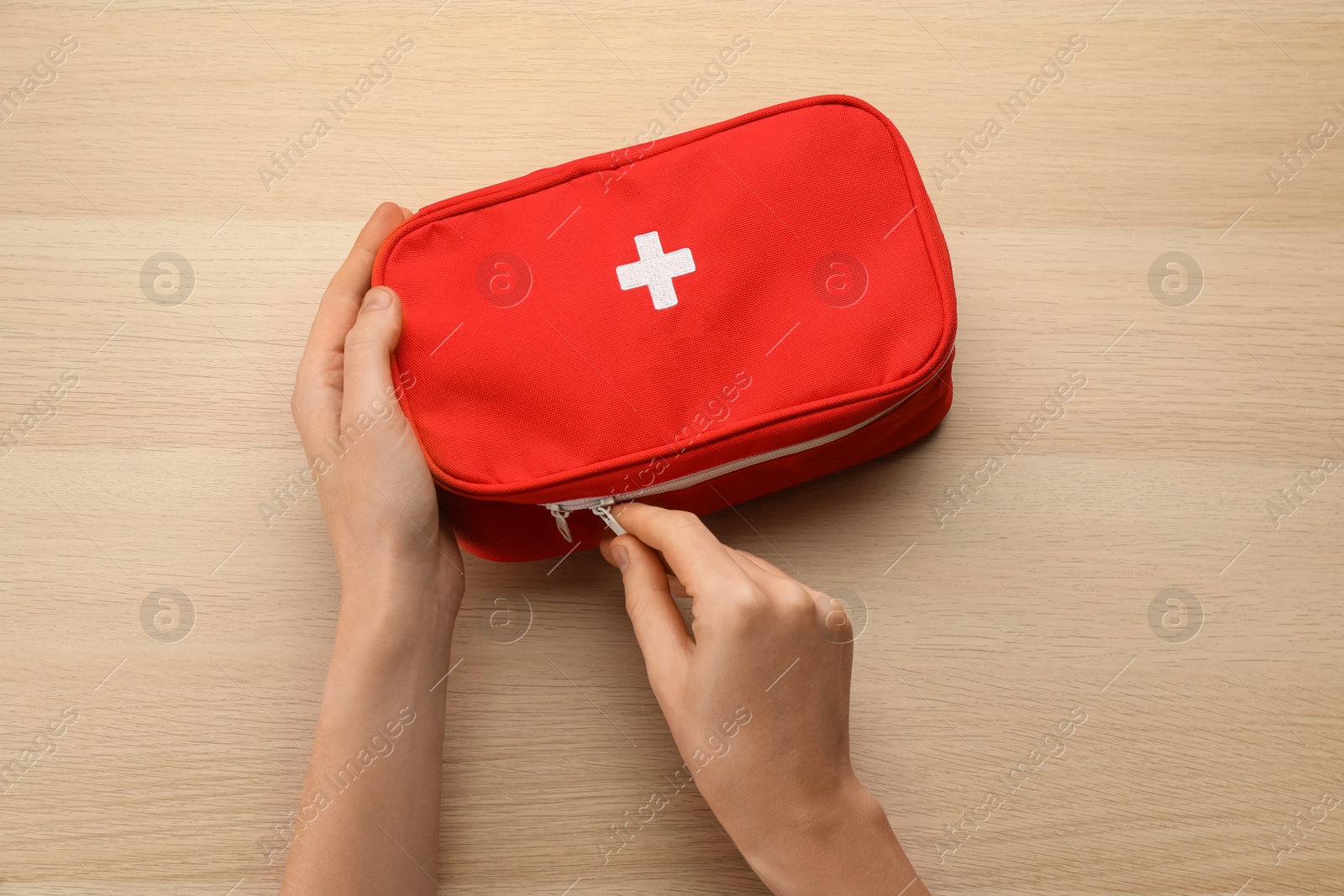 Photo of Woman opening first aid kit bag at light wooden table, top view