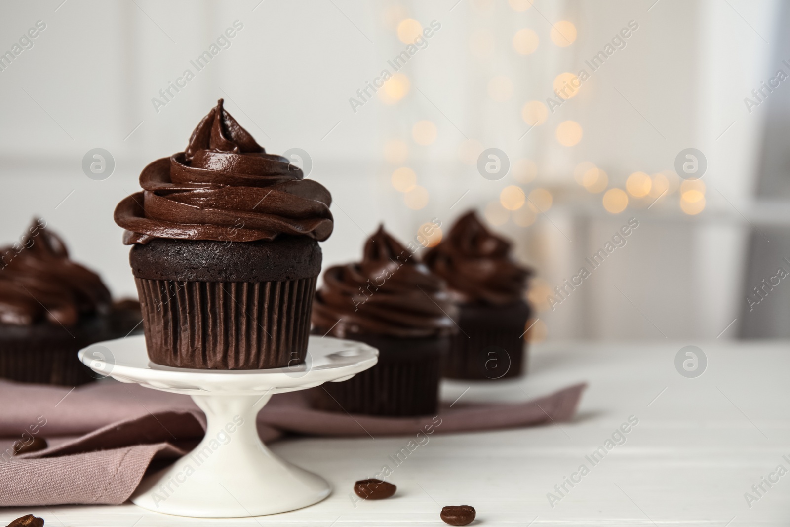 Photo of Dessert stand with delicious chocolate cupcake on white table against blurred lights. Space for text