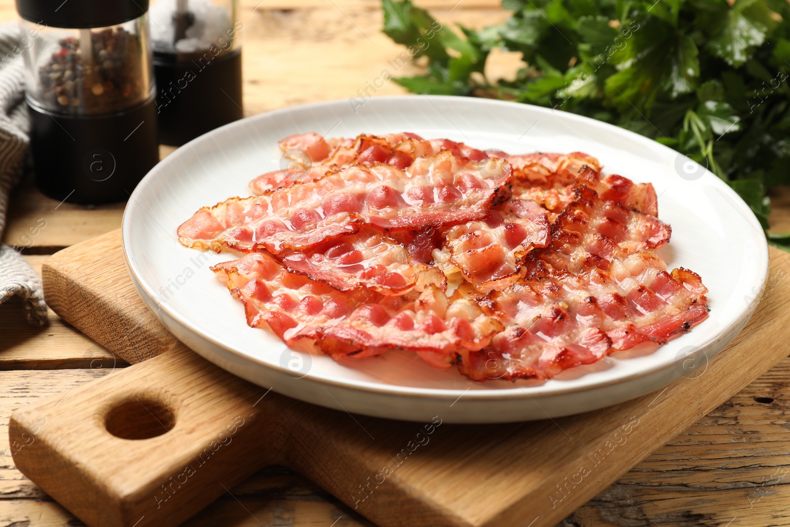 Photo of Plate with fried bacon slices on wooden table, closeup